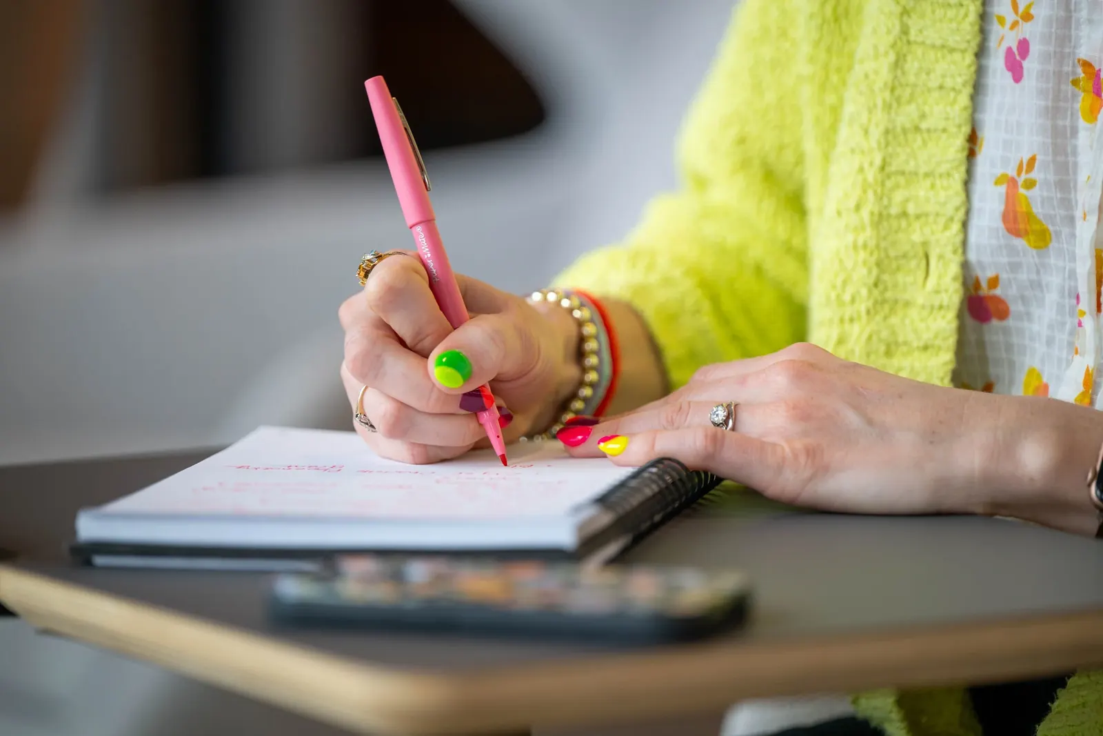 Hands writing notes in a planner beside a laptop